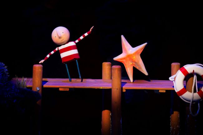 A puppet of a boy in a red and white striped jumper. He is on a pier, next to him is a shining star. Text reads 'How to Catch a Star'. 